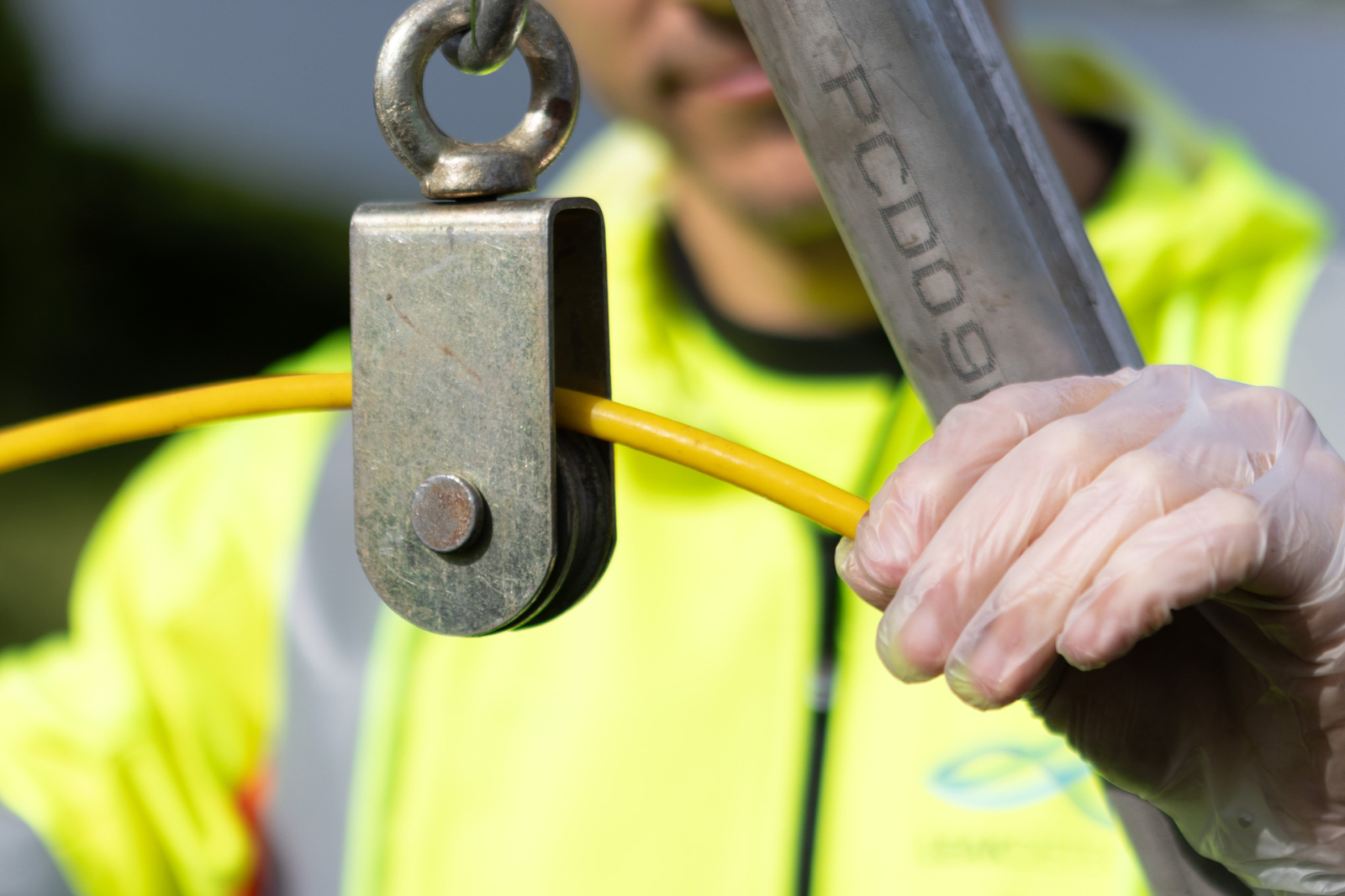 Hånd med hanske holder gul kabel gjennom metalltrisse ved avløpsarbeid
