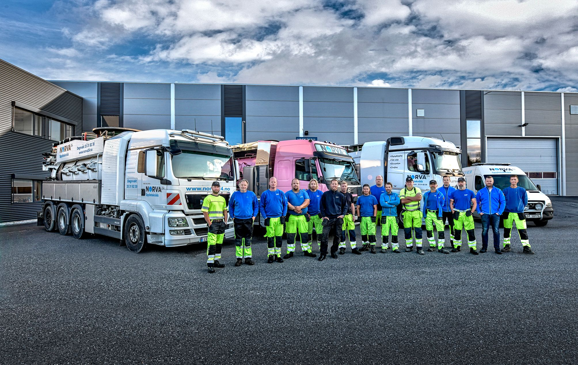 Norva24-Team in Arbeitskleidung posiert mit der LKW-Flotte des Unternehmens im Depot