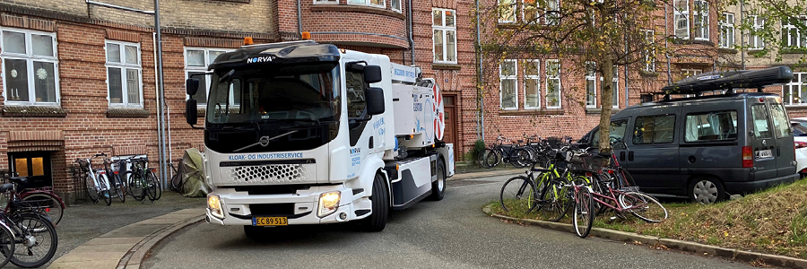 En Norva24 el-lastbil kører gennem et boligområde med cykler og parkerede biler