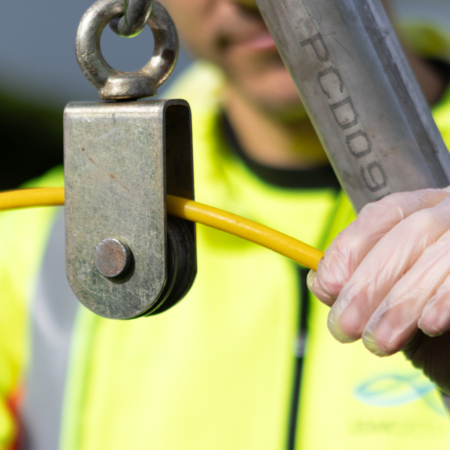 Hånd med hanske holder gul kabel gjennom metalltrisse ved avløpsarbeid