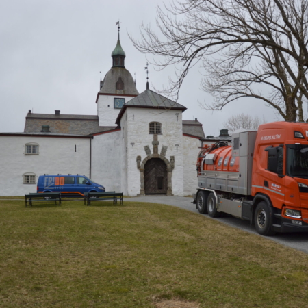 Oransje lastebil foran et hvitt slott med grønn kuppel og blå varebil.