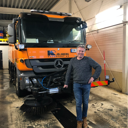 Mann i genser som står foran en oransje Kjelsberg gatefeiebil.