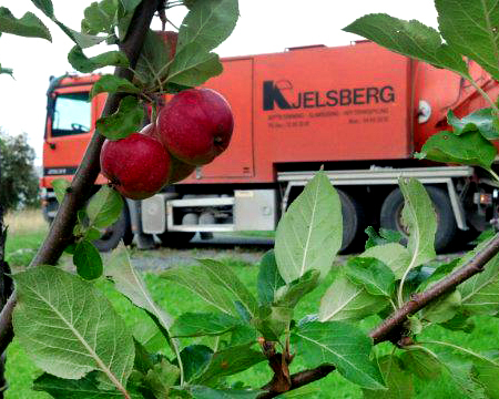 Røde epler på en tregren med en oransje Kjelsberg-lastebil i bakgrunnen.
