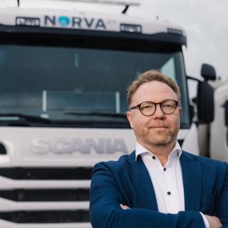 Man i glasögon står självsäkert med armarna i kors framför en vit Norva24-lastbil.