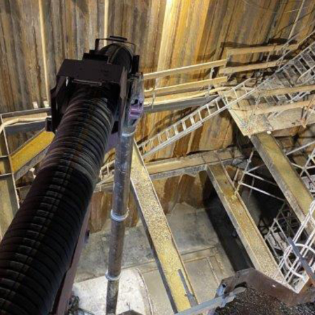 Stort industriellt vakuumrör som arbetar i ett djupt schakt med byggställningar och stegar.
