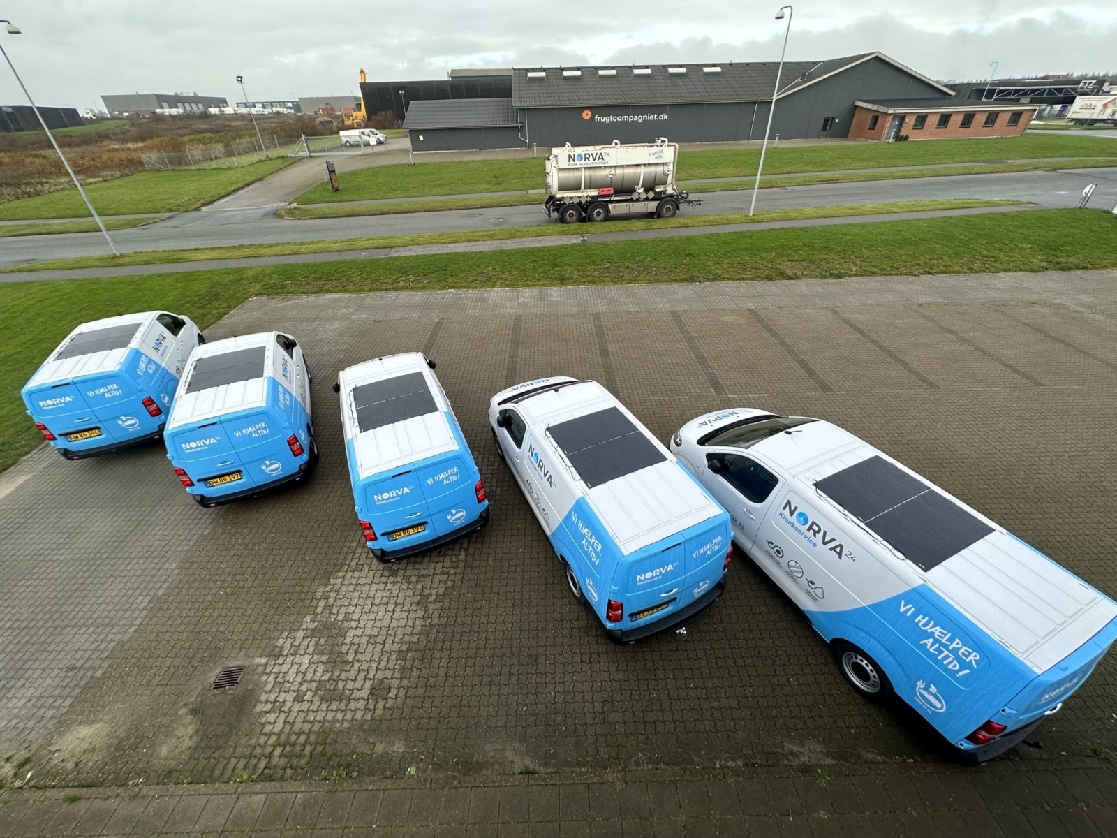 Fem Norva24 servicevogne med blå og hvid branding set ovenfra på en parkeringsplads.