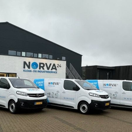 Fem varumärkta Norva24-servicebilar parkerade framför en företagsbyggnad en molnig dag.