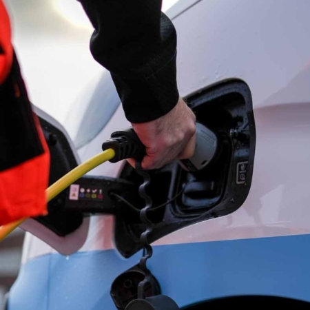 Person laddar en elbil med en gul kabel vid en laddstation.