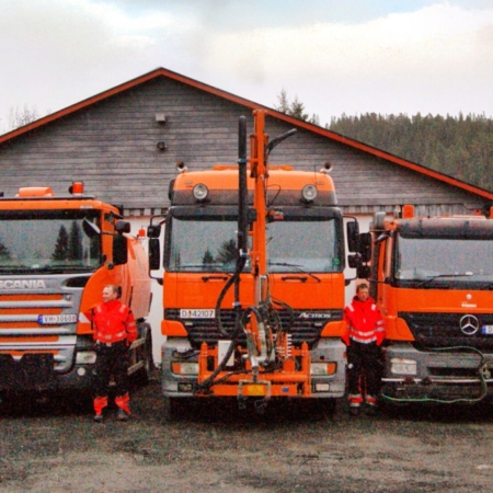 Workers posing by orange and white utility trucks outside a wooden garage.