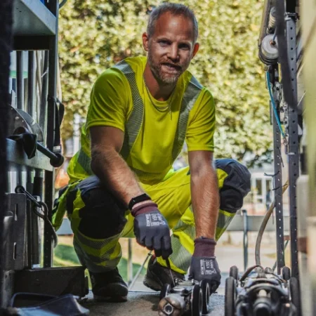 En arbetare i varselkläder knäböjer i en servicebil och hanterar verktyg.