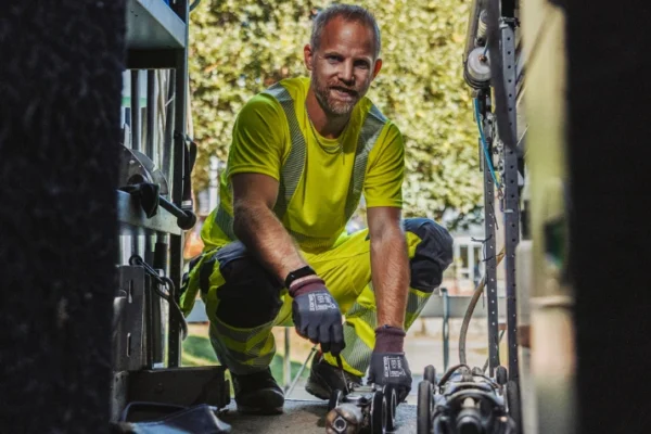 En arbetare i varselkläder knäböjer i en servicebil och hanterar verktyg.