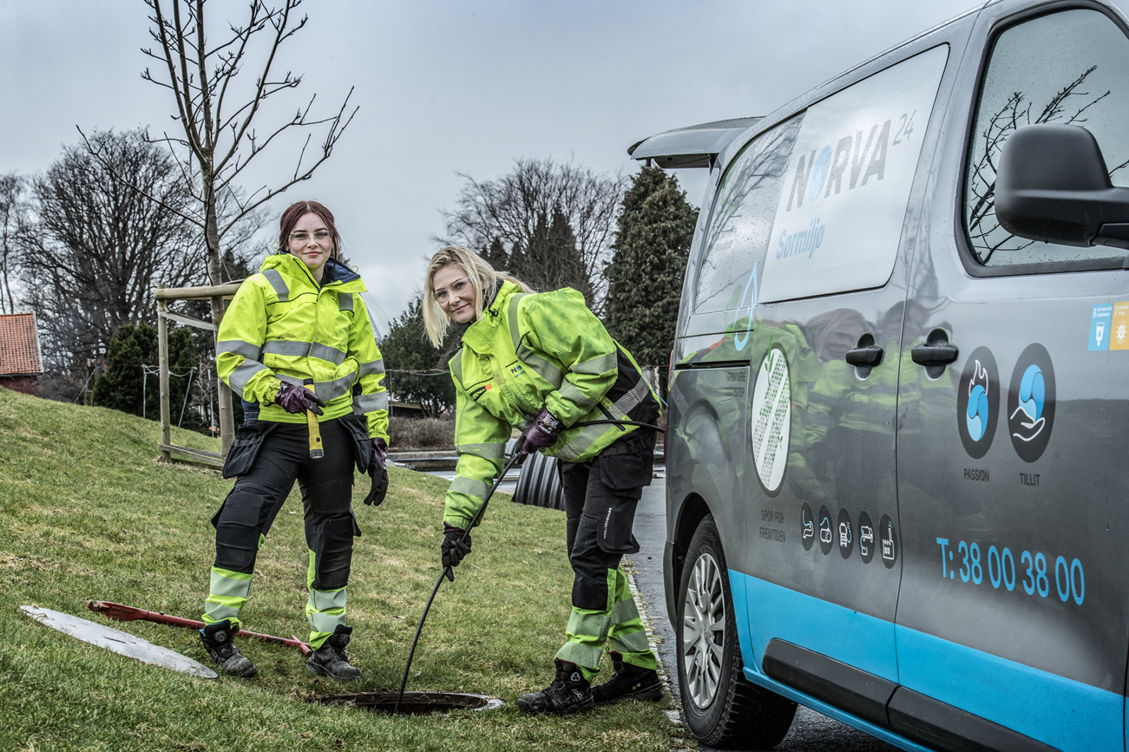 To arbeidere inspiserer et kloakkanlegg med verktøy ved siden av en Norva24-servicebil på et gresskledd område