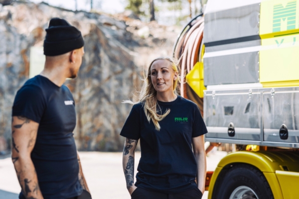 Två arbetare i svarta tröjor pratar bredvid en gul lastbil utomhus