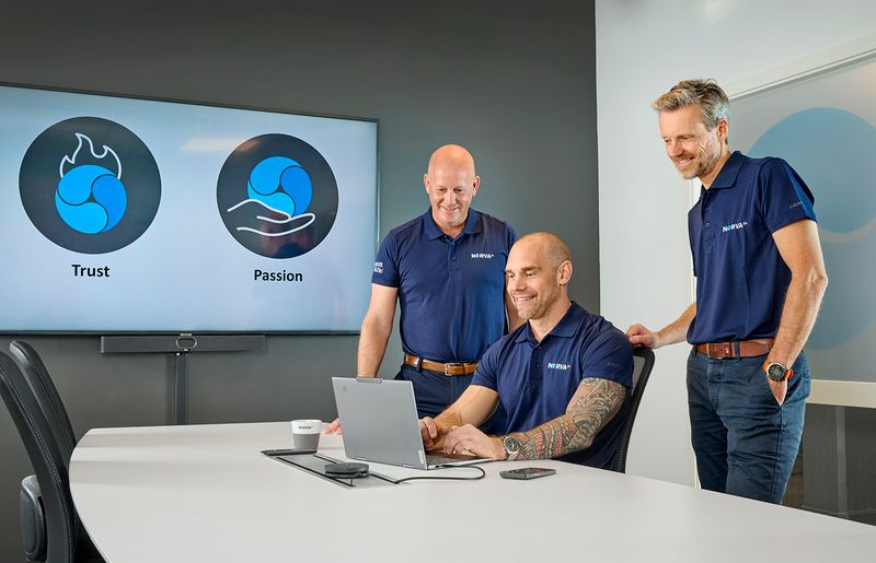 Tre Norva24-anställda samarbetar vid en laptop i ett mötesrum