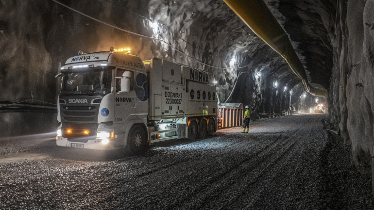A vacuum truck performing cleaning operations inside a dimly lit tunnel with a worker monitoring.