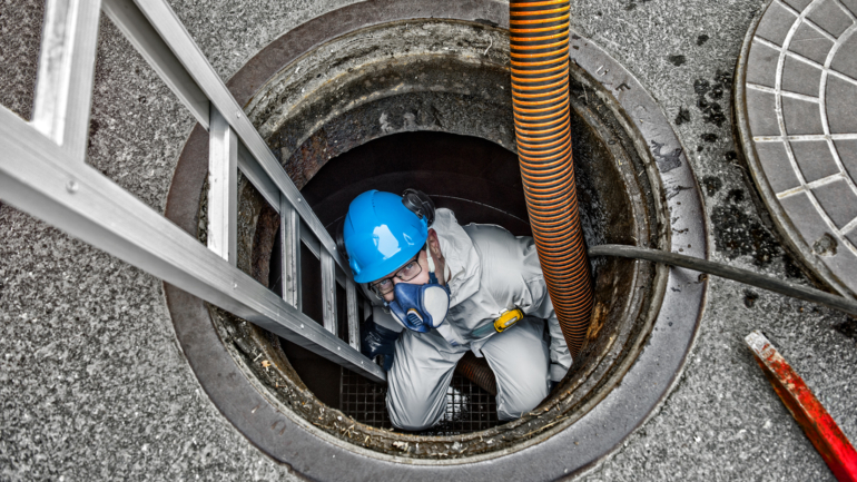 Worker in protective gear performing maintenance inside a tank.