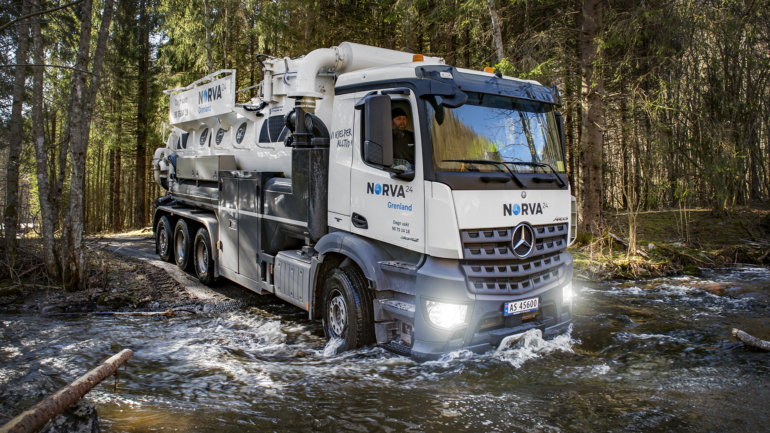 Vacuum truck crossing a stream to perform cleaning tasks in a forest.