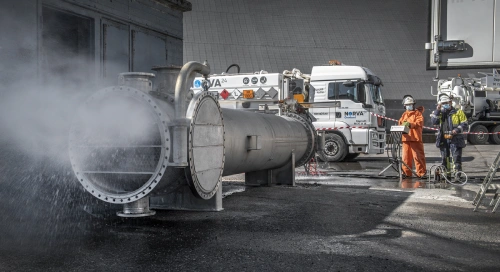 High-pressure water cleaning on metal pipe with workers in protective gear