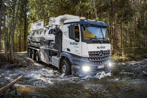 Vacuum truck crossing a stream to perform cleaning tasks in a forest.