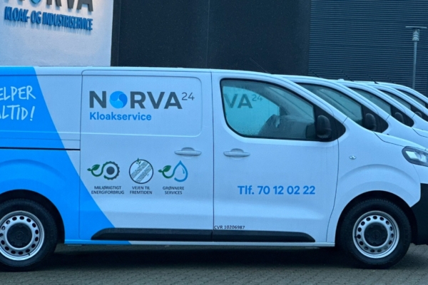 Norva24 electric vans parked in front of a building with a sign, featuring environmental and service graphics.