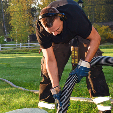 Worker in safety gear handling a large suction hose for outdoor septic tank maintenance.