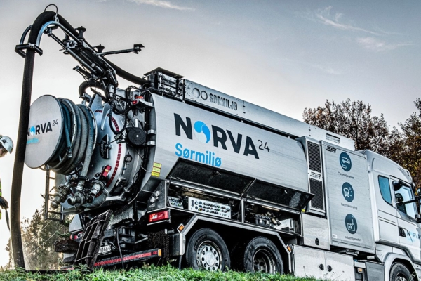 Worker in high-vis suit operating NORVA24 vacuum truck on grassy roadside