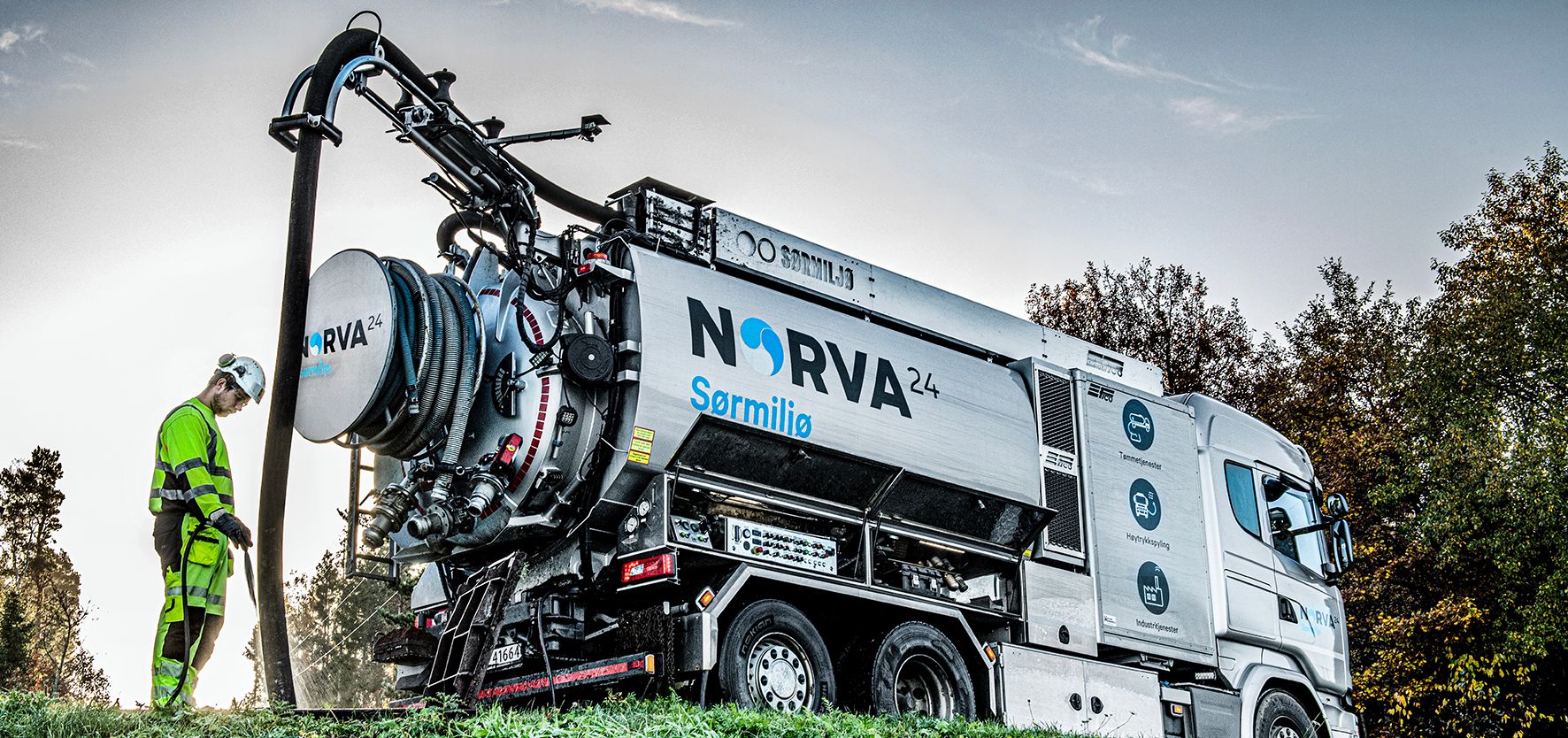Worker in high-vis suit operating NORVA24 vacuum truck on grassy roadside