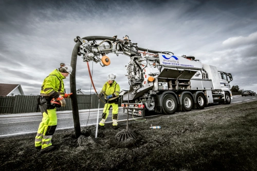 Workers in hi-vis gear operate vacuum truck cleaning pipelines by roadside