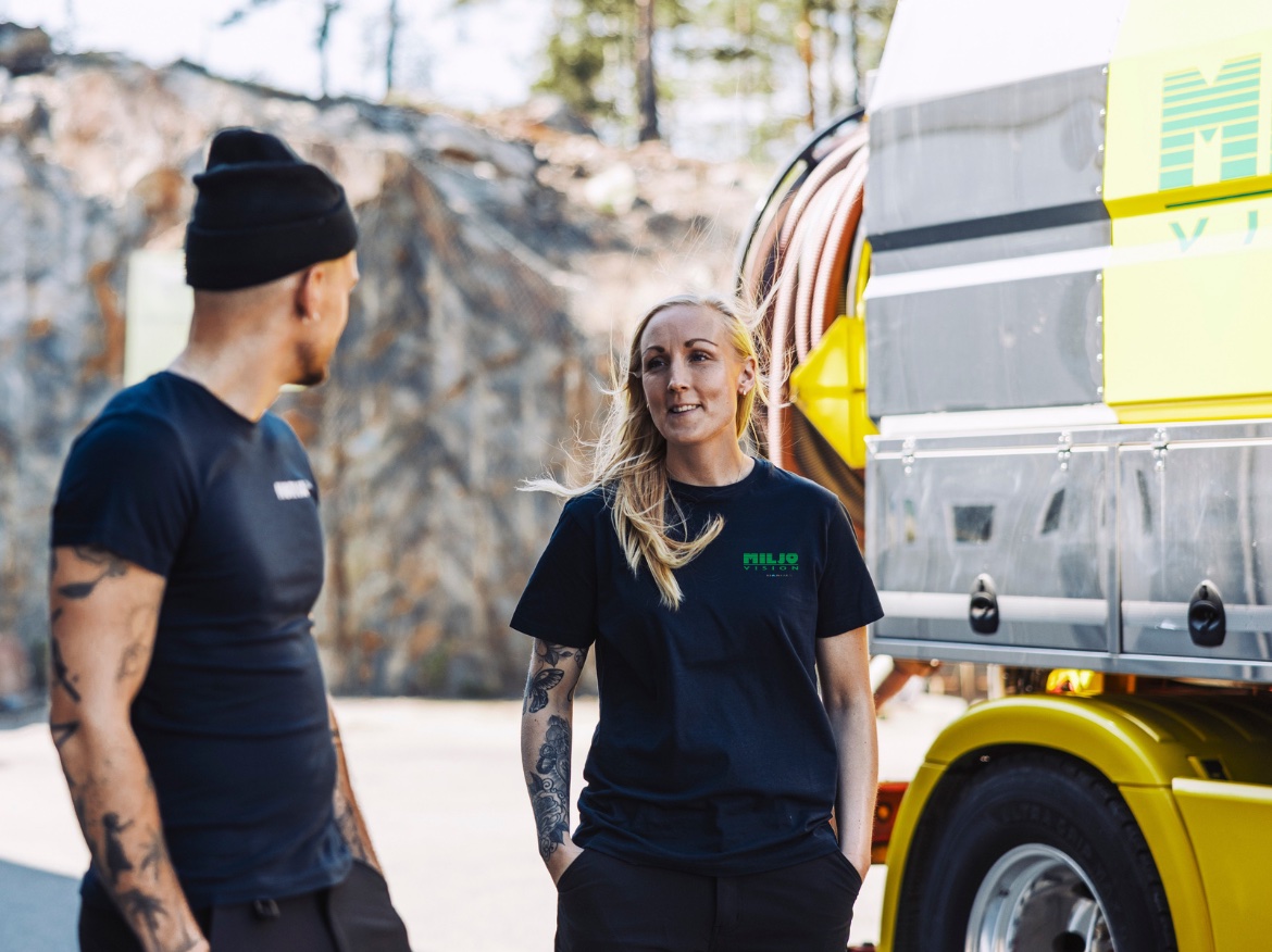 Two workers in black shirts talking next to a yellow truck outdoors