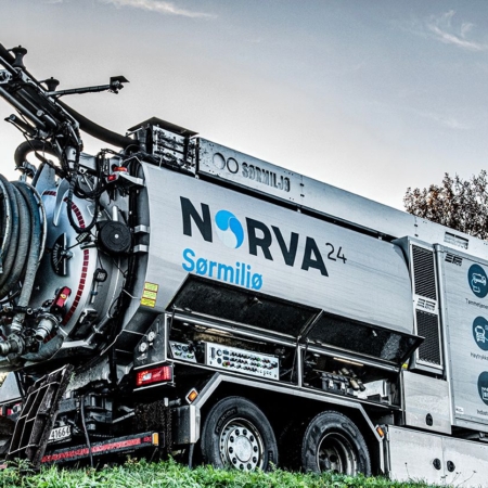 Worker in high-vis suit operating NORVA24 vacuum truck on grassy roadside