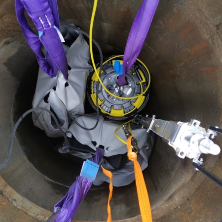 Sewer inspection camera equipment with purple lifting straps lowered into manhole